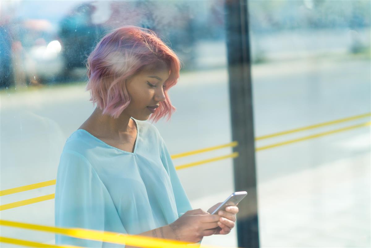 Portrett av jente i busskur som ser på telefonen sin. Foto. - Click for large image