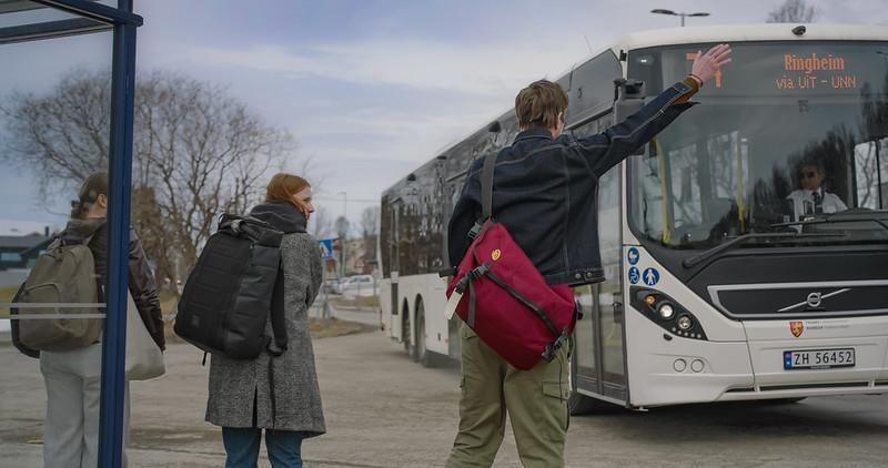 Fotografi av passasjer som står på holdeplass og gir stoppsignal til bussen - Klikk for stort bilde