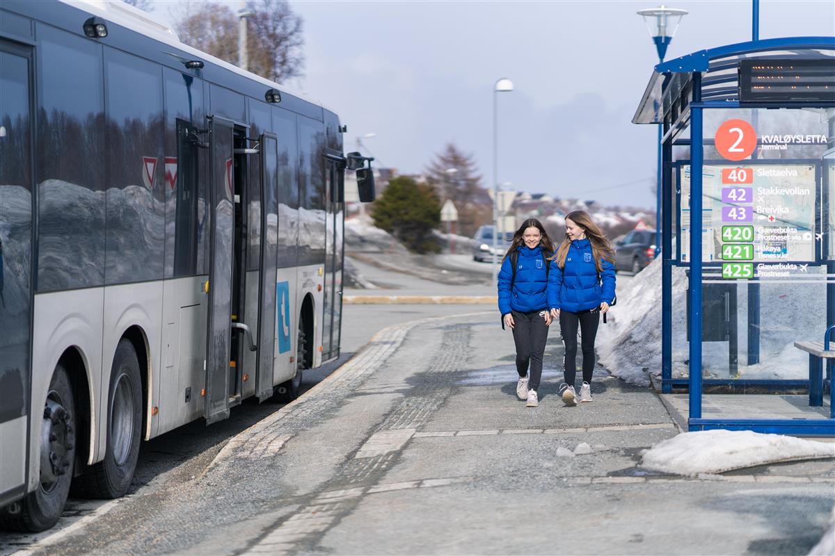Buss og to jenter ved holdeplass - Klikk for stort bilde