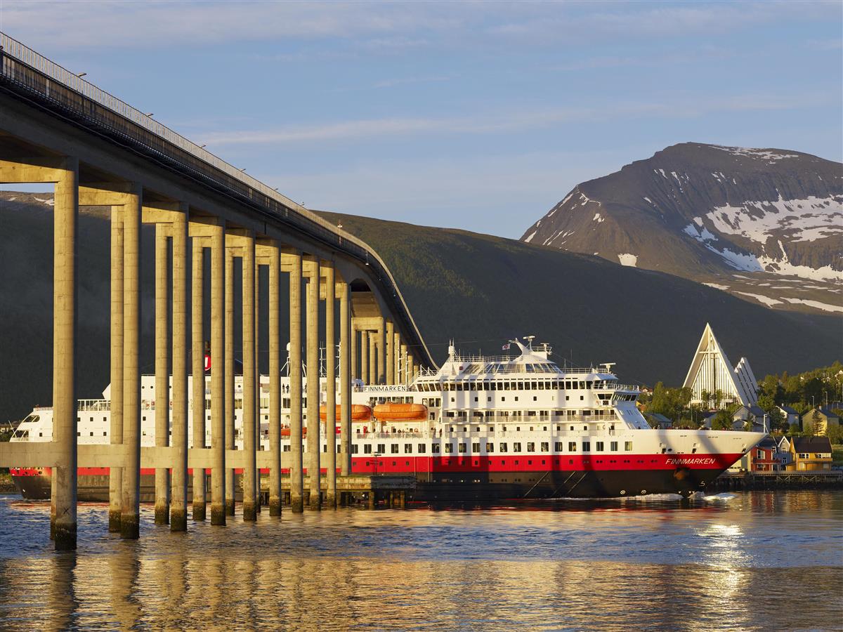 Hurtigruten under Tromsøybrua på vei inn til Tromsø. Ishavskatedralen og solfylte fjell i bakgrunnen. Foto. - Klikk for stort bilde