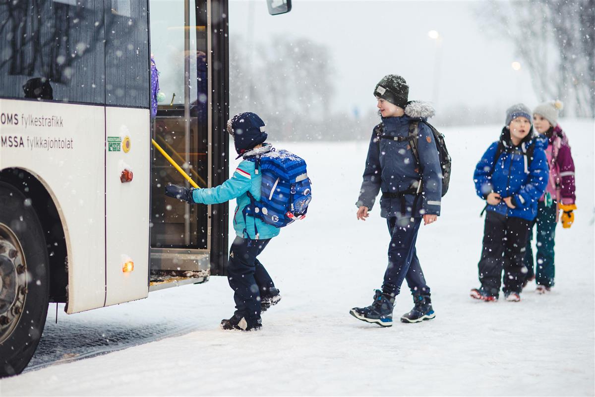 Bilde av barn som går ombord i en buss i snøvær. Foto. - Klikk for stort bilde